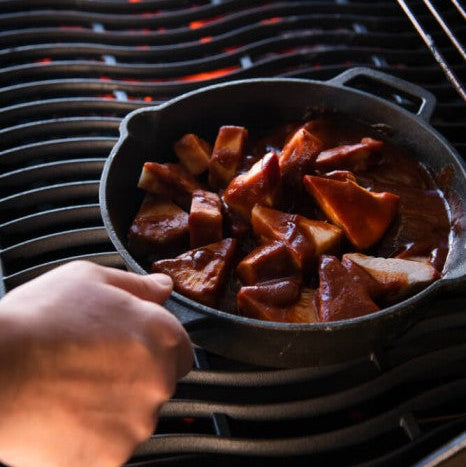 Person holding a cast iron skillet with food over an open flame