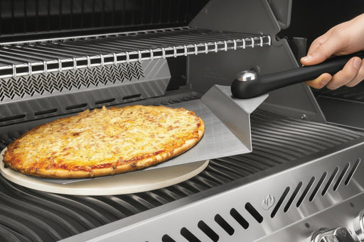 Grilled pizza being removed from a barbecue grill using a pizza peel.